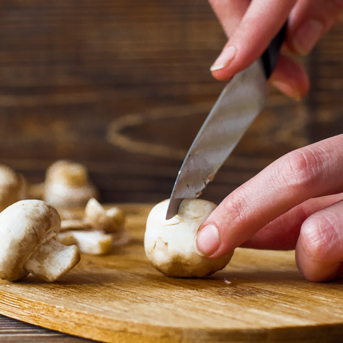 Cook hand slicing mushrooms on cutting board