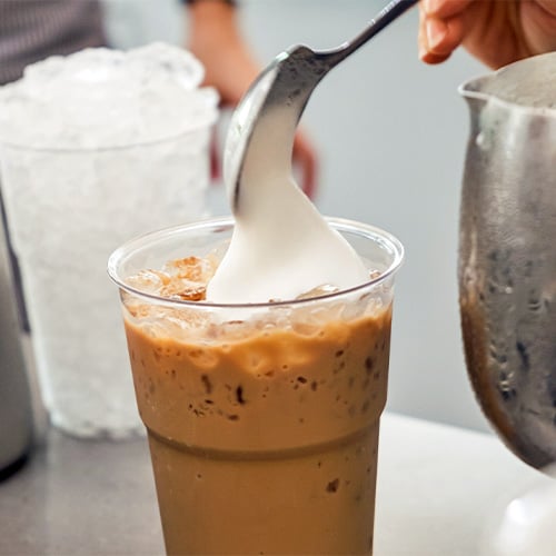 Cold foam being spooned onto coffee drink