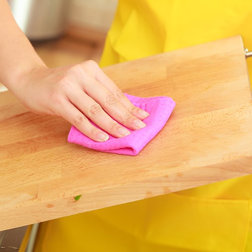 pink cloth wiping down a wood cutting board