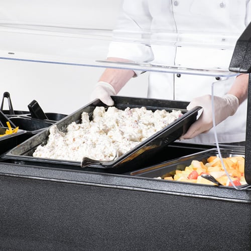 potato salad being placed into a buffet table