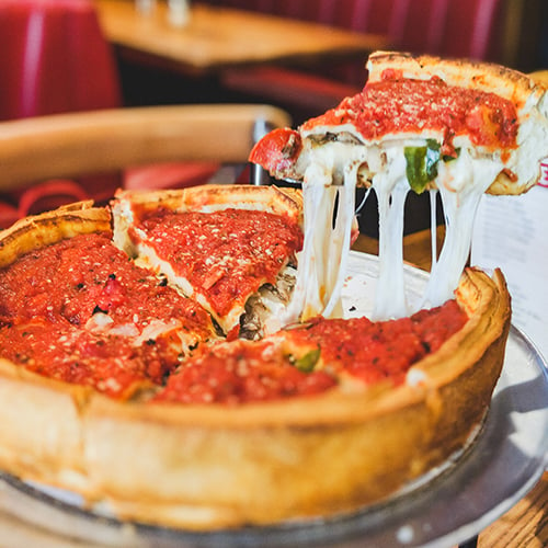 slice of deep dish pizza being pulled from pizza with cheese stretching from bottom of slice