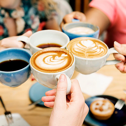 mugs of coffee with latte art on top being clinked together by guests