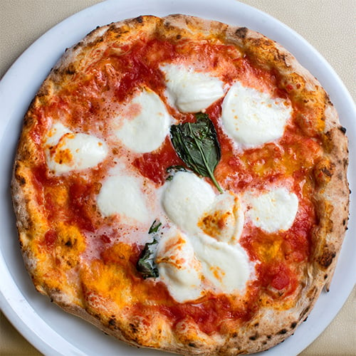 close-up view of slice of Neapolitan pizza with cheese, sliced tomatoes, and basil