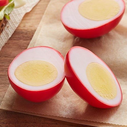 Pickled red beet eggs sliced open on a wooden cutting board