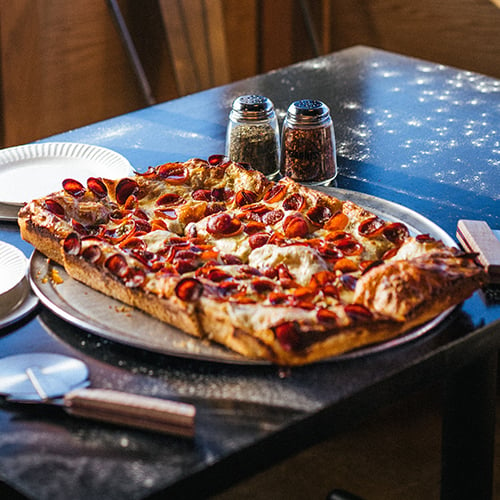 Sicilian pizza on pizza peel with beers next to it