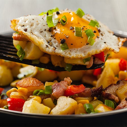 Sunny Side Up Egg being placed on breakfast potato hash