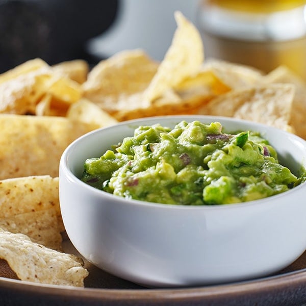 Bowl of guacamole with chips in the background