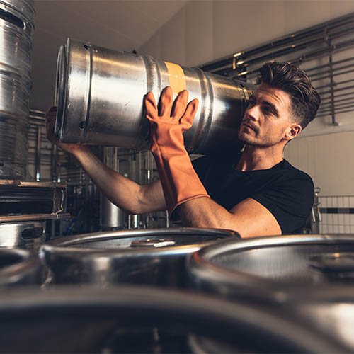 Brewer carrying metal beer barrel at brewery factory