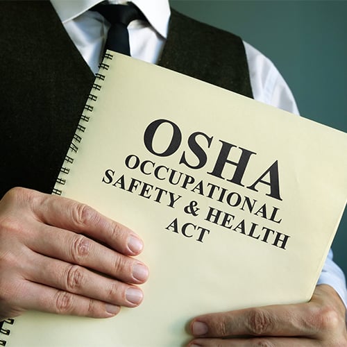 hands holding a booklet that reads 'OSHA - Occupational Safety and Health Act'