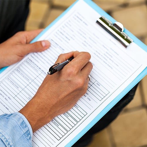 hand filling out printed report form on a clipboard