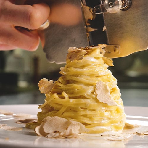 Man shaving truffle onto pasta