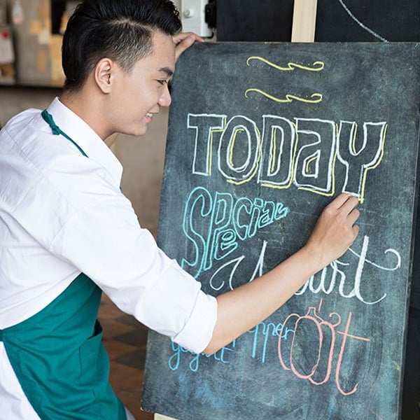 young bar employee writing daily specials on a chalk board sign
