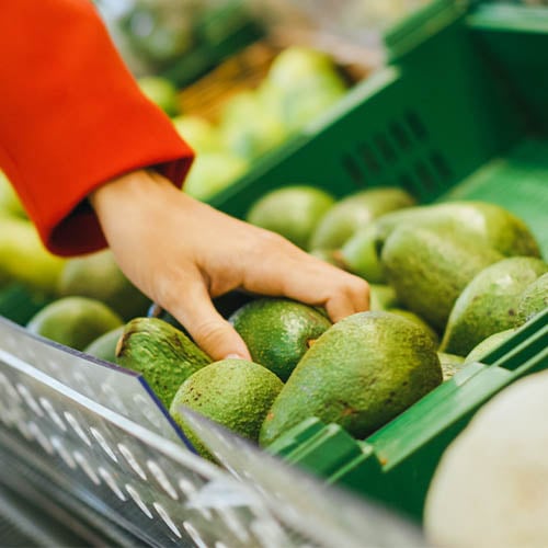 person reaching for avocado in grocery store