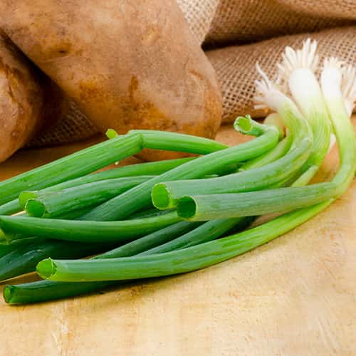 Scallions on a cutting board with a potato