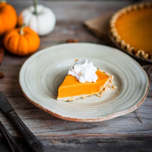 slice of pumpkin pie on a plate with pumpkins on a table