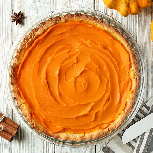 top view of a pumpkin pie on a white table with spices scattered around