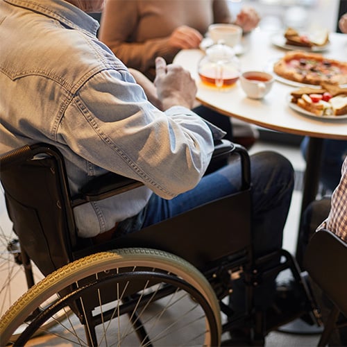 Man in wheelchair surrounded by friends sitting at table 