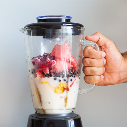 Hand holding handle of a blender full of fruits and milk