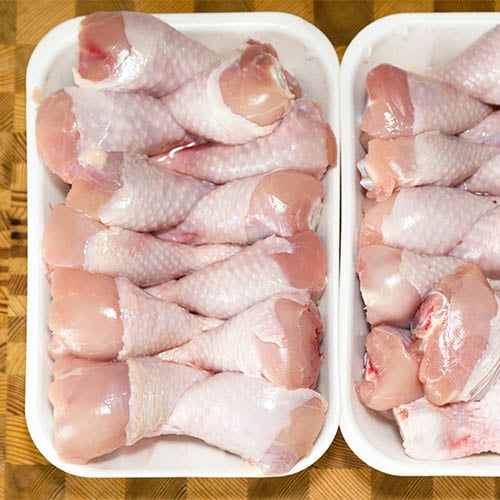 raw chicken drum sticks sitting in white container