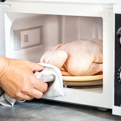 Hand placing frozen chicken into microwave