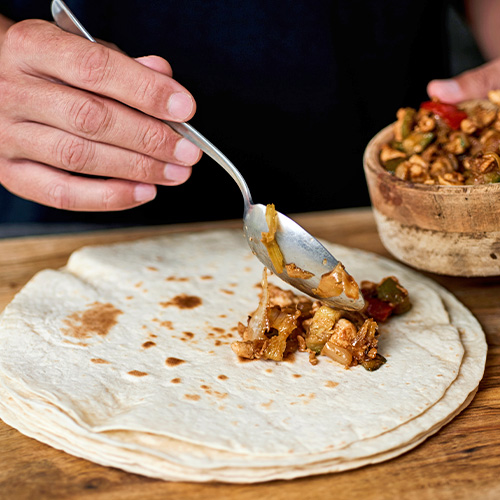 person putting cooked chicken on tortilla