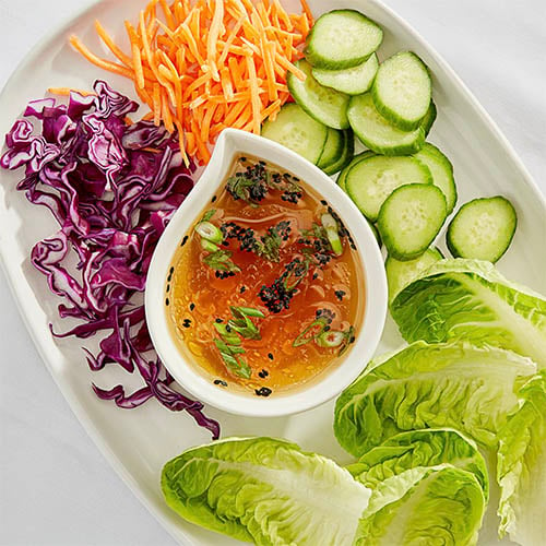 fish sauce in a white dipping bowl in the middle of a tray of fresh vegetables for lettuce wraps