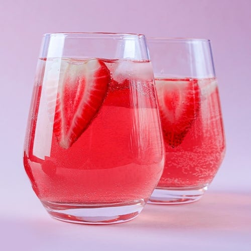 Two glasses of Strawberry Rose Sangria on a light pink background with strawberries in the glasses