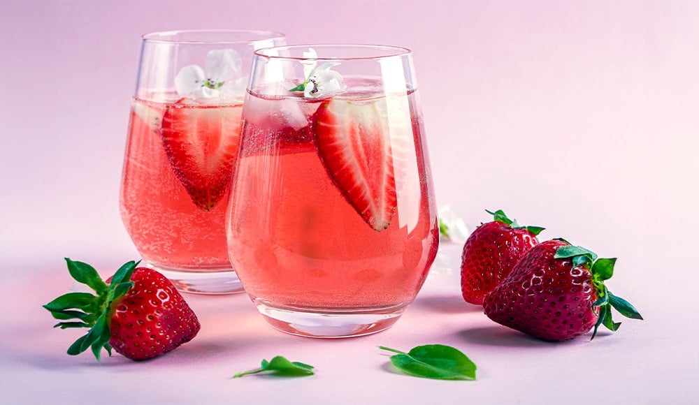 Two glasses of Strawberry Rose Sangria with strawberry garnishes sitting on a pink surface surrounded by strawberries