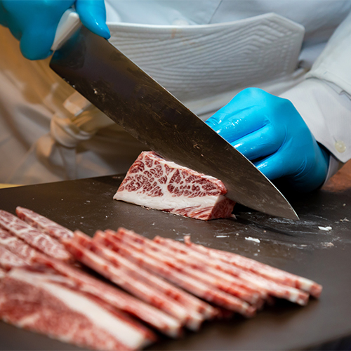 closeup of hands slicing wagyu steak into thin strips