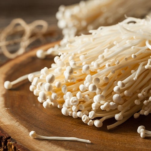 raw organic enoki mushrooms on a round cut of wood