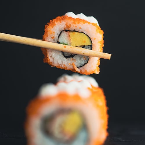 close up view of a piece of sushi held up by chopsticks