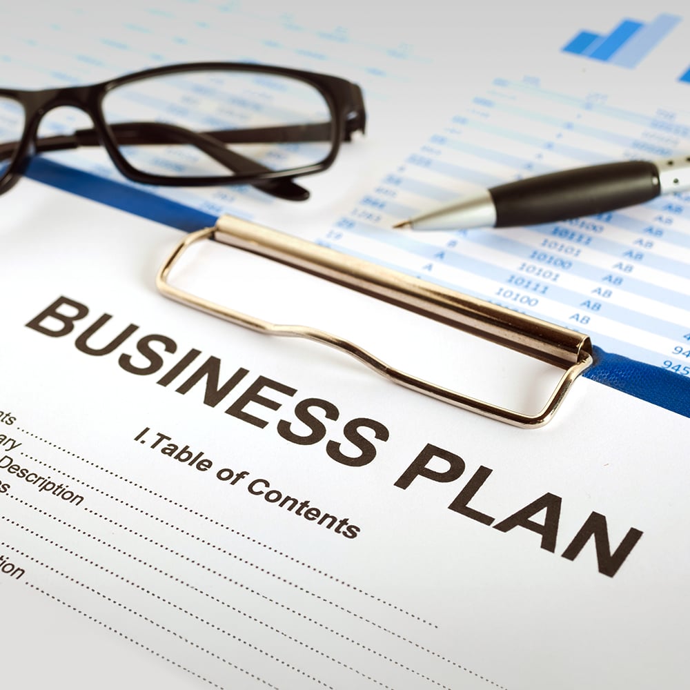 business plan on clipboard with pen and glasses