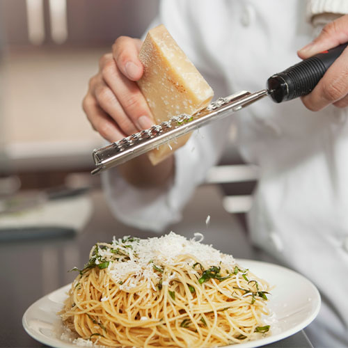Chef grating cheese over pasta