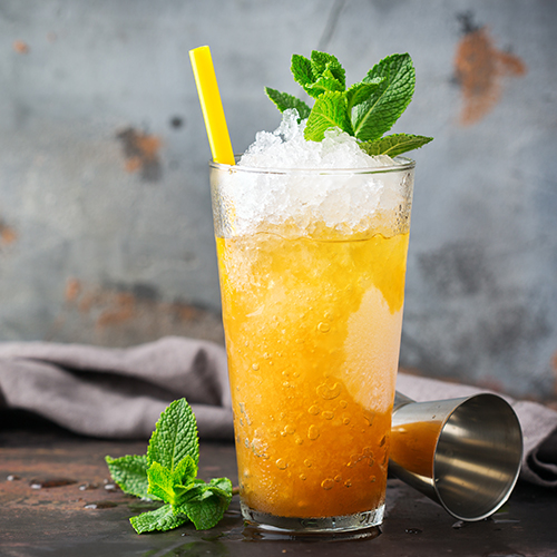 a ginger peach julep in a glass on a wooden table surrounded by a cocktail measure and mint leaves