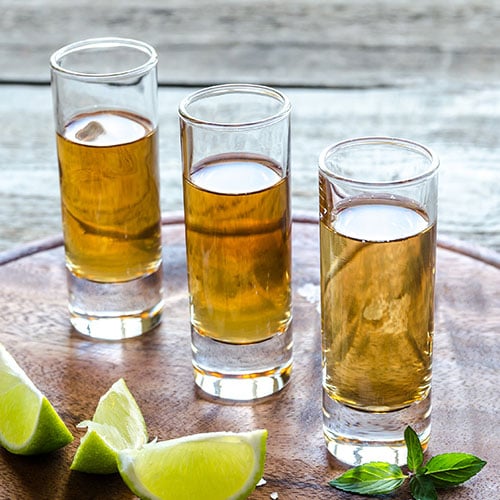 anejo tequila, a set of 3 shot glasses of tequila with lime wedges scattered in front