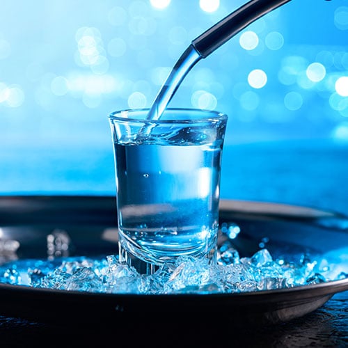 clear tequila being poured into a shot glass, blue background