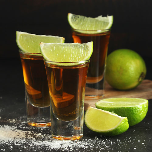 Extra Anejo tequila, a set of 3 shot glasses with lime wedges sitting on top, dark background, salt scattered around glasses
