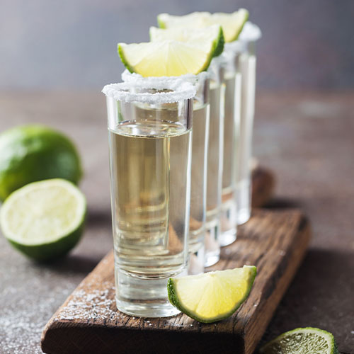 flight of Gold tequila in a set of 5 shot glasses with salt on the rim and lime wedges on the top, sliced lime in the background, salt scattered around on the table