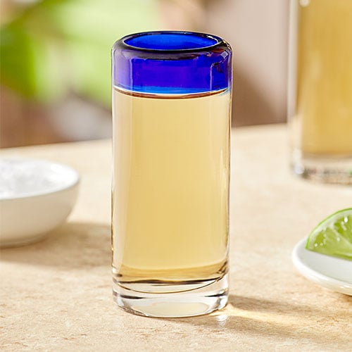 reposado tequila in decorative shot glass that has a blue rim, sitting on light colored table