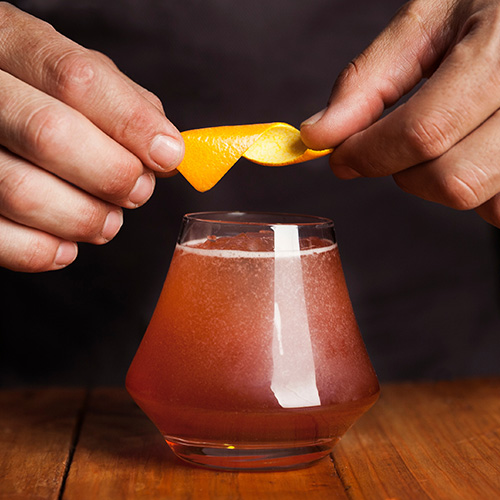 Bartender placing an orange twist on a cocktail
