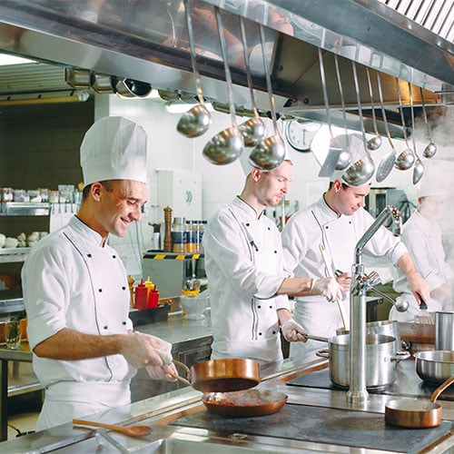 Kitchen hierarchy, 3 smiling chefs in a commercial kitchen cooking multiple dishes