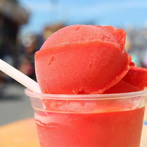 clear cup with red italian ice and a white spoon on a bright summer day
