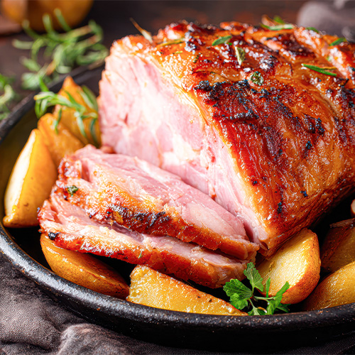 ham half on a plate with fresh rosemary and roasted potatoes