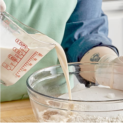 Chef pouring evaporated milk into a mixing bowl