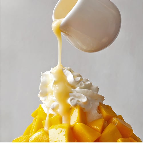 Condensed milk being poured over fresh mango and whipped cream