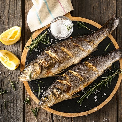 two full branzino fish served on a plate with lemon and salt