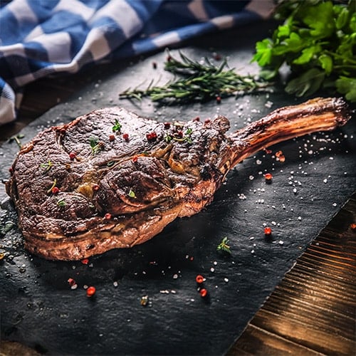 tomahawk steak on slate platter with peppercorn garnish