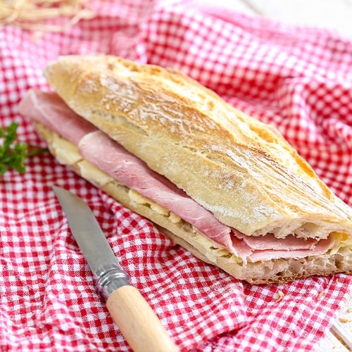 Ham sandwich on french bread laid on a red and white checkered napkin