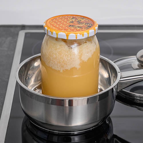 How to Decrystallize Honey with Hot Water, jar of honey in metal pot filled with water sitting on a stove