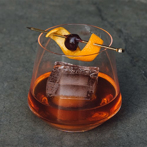 Old fashioned drink sitting on a dark countertop with a dark background
